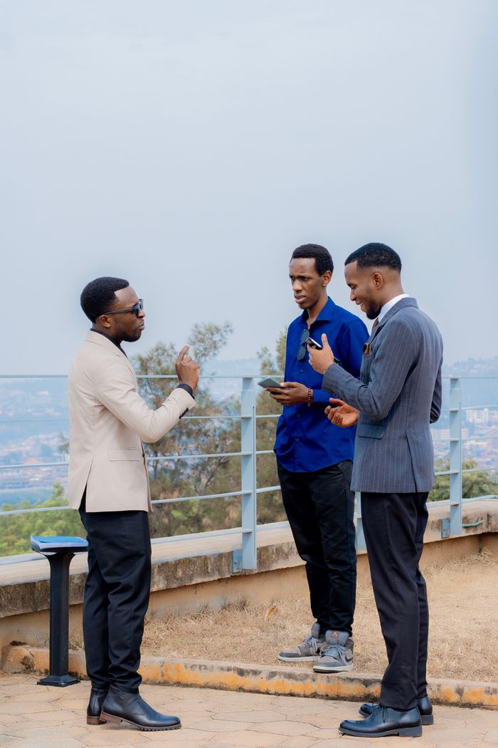 product-03 Three businessmen engage in discussion on a balcony with city views.