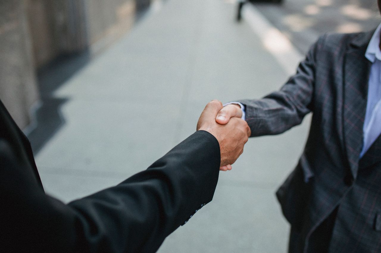 home-bg-img Close-up of two businessmen shaking hands outside, symbolizing partnership and agreement.